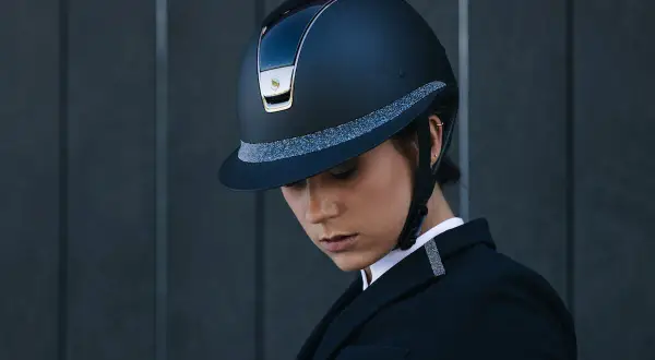 Elegancki kask marki kask, ozdobiony brokatową taśmą, noszony przez kobietę w czarnym żakiecie.