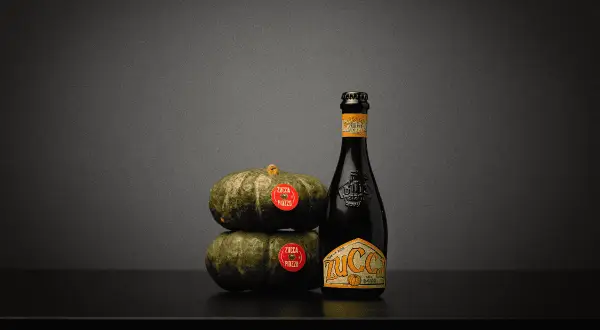 Una bottiglia di birra alla zucca accanto a due zucche impilate.