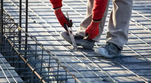 Budowlaniec wiąże zbrojenie, szacując, ile stali na fundament 100m2 będzie potrzebne.