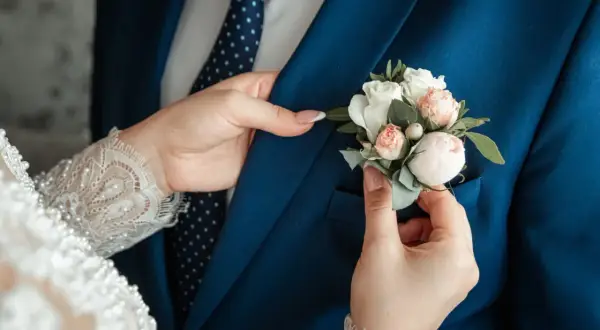 Les mains de Caroline ajustent la boutonnière sur le costume bleu du marié. Un moment tendre avant leur mariage à l'hôtel.