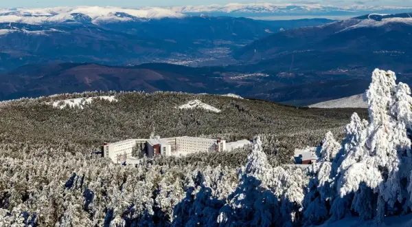 Edificio hotelero en la cabeza de Manzaneda, rodeado de pinos nevados y montañas al fondo.
