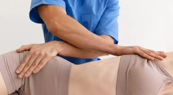 Fizjoterapeuta wykonuje masaż biodra, łagodząc mrowienie. Dłonie terapeuty obejmują okolicę biodrową pacjentki.