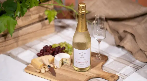 Niemieckie wino musujące "Deutscher Sekt" na desce z serami, winogronami i kieliszkiem. Idealne na letnie popołudnie.