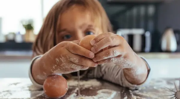 Kind mit bemehlten Händen knackt Eier. Vorsicht vor salmonellen eiern, besonders bei rohem Verzehr.