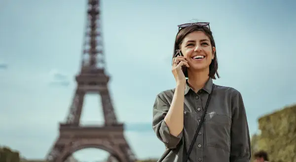 Uśmiechnięta kobieta rozmawia przez telefon w Paryżu, niedaleko Wieży Eiffla. Dowiedz się, jak uruchomić roaming w Play, by cieszyć się rozmowami za granicą.