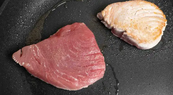 Zwei Thunfischfilets in einer Pfanne: eines roh und rosa, das andere leicht angebraten und goldbraun.