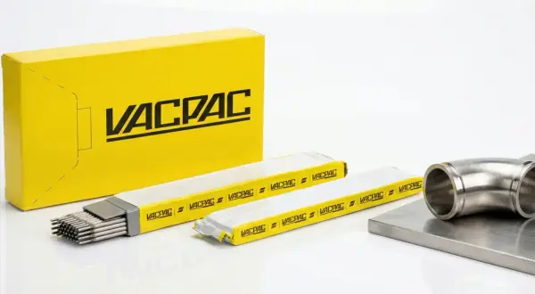 Żółte pudełko z logo VACPAC, obok opakowania z elektrodami spawalniczymi i metalowym kolankiem.