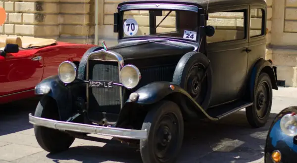 Auto storica nera, un vero gioiello che dimostra quanti anni ha un'auto d'epoca. Accanto, un'auto rossa sportiva.