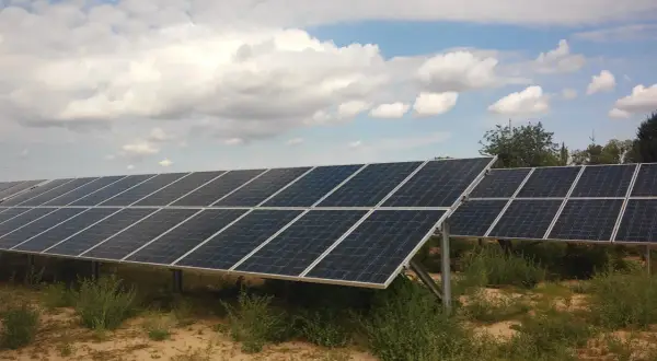Rzędy paneli fotowoltaicznych na tle błękitnego nieba z chmurami. Firma oferuje sprzedaż energii z fotowoltaiki.