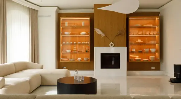Nowoczesny salon z kominkiem, przeszklonymi witrynami z zastawą i beżową sofą.