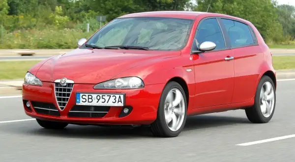 Czerwona Alfa Romeo 147 w ruchu, z widocznymi reflektorami i grillem.