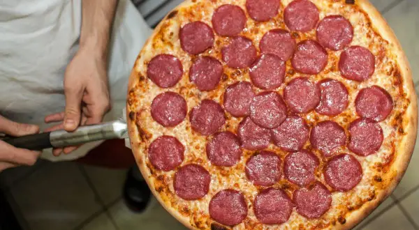 Pizza z salami na łopacie, trzymana przez kucharza.