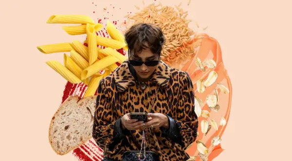 Frau im Leo-Mantel checkt ihr Handy, umgeben von Nudeln, Brot, Reis und Haferflocken. Sie fragt sich, wie viel Kohlenhydrate am Tag gesund sind.