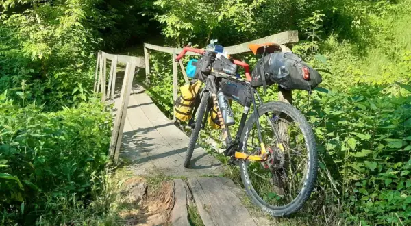 Rower wyprawowy na drewnianym moście, gotowy na mazowiecki gravel. Otoczony bujną zielenią, zaprasza do przygody.