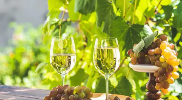 Deux verres de vin blanc frais, des grappes de raisins et un tire-bouchon sur une table en bois, parfait pour une visite à Saint-Émilion.