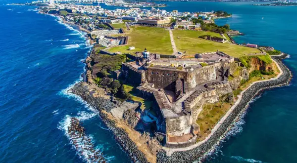 Widok na zabytkową fortecę i miasto San Juan, gdzie jest Puerto Rico. Błękitne morze otacza skaliste wybrzeże.