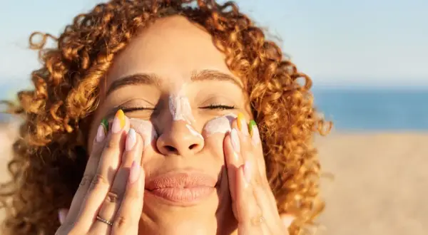 Frauenhände verteilen Sonnencreme mit Methylene bis-benzotriazolyl tetramethylbutylphenol auf der Nase.