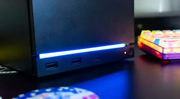 Czarny steam machine z niebieskim podświetleniem, portami USB i gniazdem na kartę SD. Obok kolorowa klawiatura.