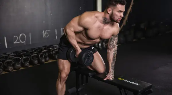 Mann macht ein Workout mit Hanteln auf einer Bank im Fitnessstudio.