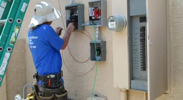 Elektryk pracuje przy skrzynce elektrycznej, podłączając przewody. To kluczowy etap instalacji, który zapewni odpowiednią moc przyłączeniową.