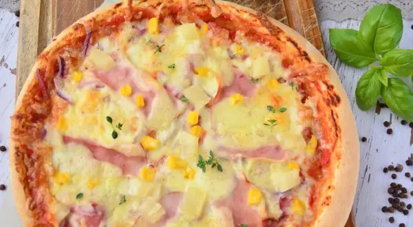 Apetyczna pizza z ananasem, szynką, kukurydzą i serem, ozdobiona świeżymi ziołami.