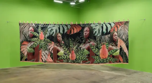 A tapestry at little April Galleries features four portraits of women amidst lush tropical foliage and pineapples.