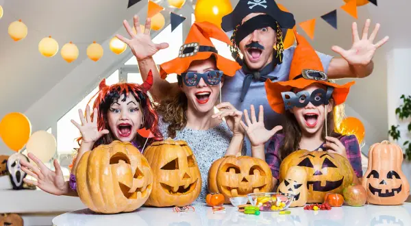 Famille costumée, joyeuse, prête à organiser soirée d'Halloween avec citrouilles sculptées et bonbons.