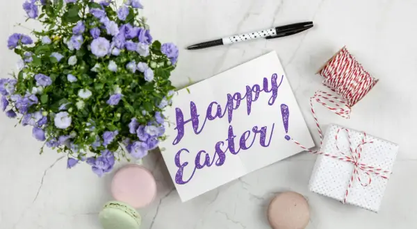 Wielkanocne słówka po angielsku: "Happy Easter!" na kartce, obok kwiatów, makaroników i prezentu.