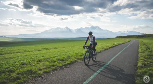 Kobieta na rowerze przemierza malowniczą trasę z widokiem na ośnieżone Tatry. To idealne miejsce na **velo tatry** i podziwianie krajobrazów.