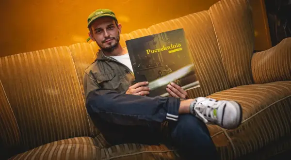 Młody mężczyzna w czapce z daszkiem siedzi na kanapie, trzymając w rękach płytę Vito Bambino "Poczekalnia".