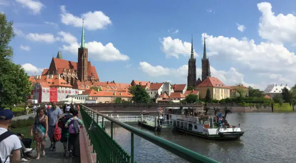 Mosty i katedra to to, z czego słynie Wrocław. Ludzie spacerują po moście, podziwiając widok na rzekę i zabytkową architekturę.
