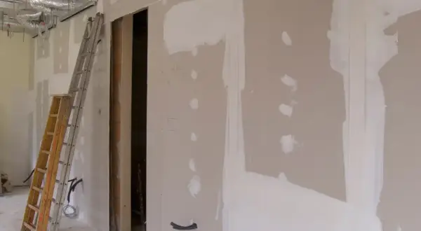 Scianka dzialowa z plyty kartonowo gipsowej w trakcie prac. Widoczne drabiny, instalacje i otwór drzwiowy.