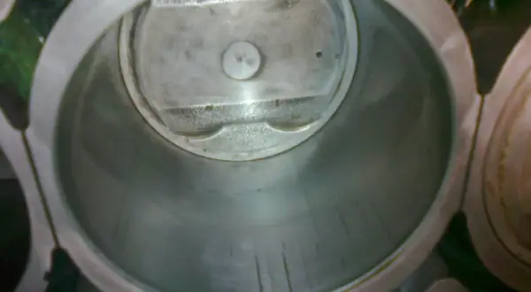 Wnętrze cylindra silnika z widocznym tłokiem. Widać ślady zużycia na ściankach, sugerujące dopuszczalny luz tłoka w cylindrze.