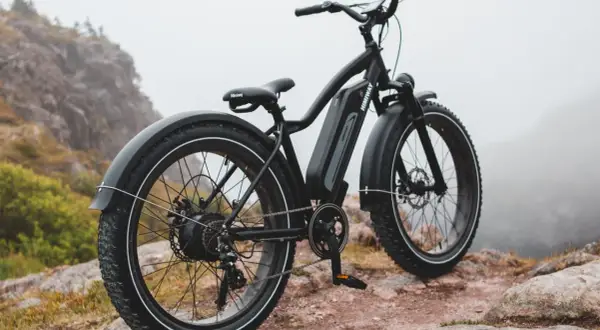 Czarny rower elektryczny z grubymi oponami na skalistym podłożu. Idealny do trudnego terenu, mógłby znaleźć się w czołówce rankingu rowerów elektrycznych.