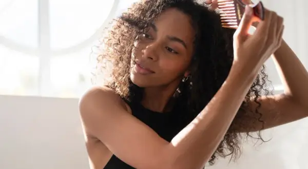 Mujer peinando su hermoso pelo colocho con un peine de dientes anchos, disfrutando de la luz natural.