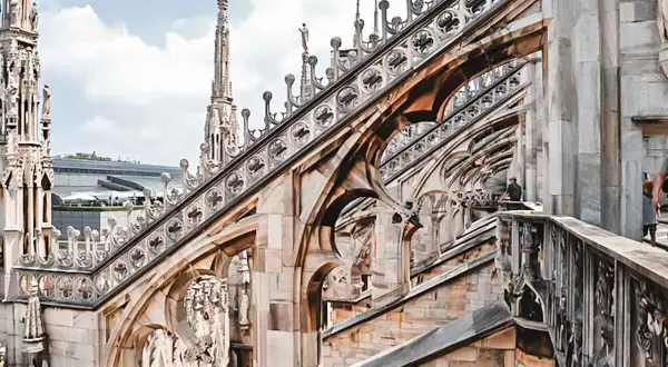 Gotycka architektura Duomo, z której słynie Mediolan, z detalami rzeźb i iglicami na tle błękitnego nieba.