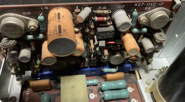 Wnętrze starego urządzenia elektronicznego z widocznymi kondensatorami, rezystorami i tranzystorami. Jeden z kondensatorów ma oznaczenie 220uF, a obok niego widać potencjalny problem z dc offset.