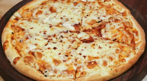 Pyszna pizza bez drożdży, obficie posypana serem i płatkami chili, pokrojona na kawałki.