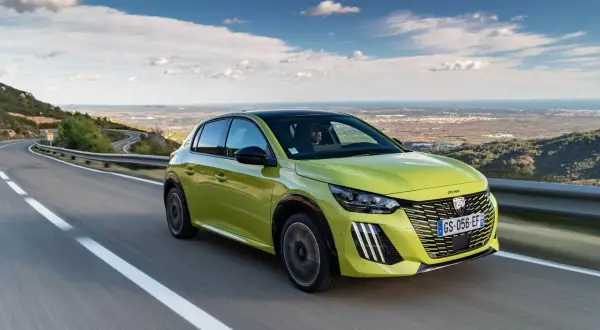 Jaskrawozielony Peugeot 208 na krętej drodze z widokiem na morze. Czy wady i zalety tego modelu skłonią Cię do zakupu?