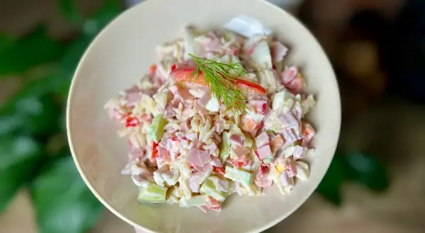 Pyszna sałatka z makaronem orzo, z szynką, jajkiem i warzywami, udekorowana gałązką koperku.