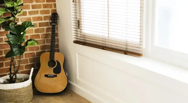 Akordy gitara klasyczna, instrument oparty o ceglaną ścianę, obok doniczki z rośliną.