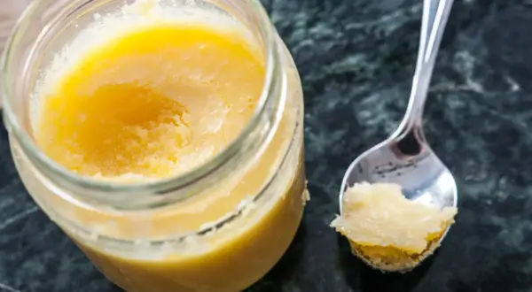 En burk med gyllene ghee och en sked med lite av det. Perfekt för ditt ghee recept!