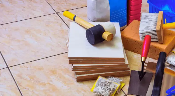 Outils pour coller du carrelage avec du ciment : carreaux, maillet, truelle, éponges, brosse, croisillons et sacs de ciment.