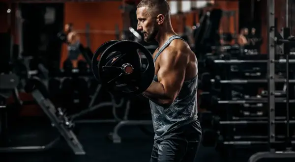 Siłacz ćwiczy biceps z ciężarem, czując napięcie w tricepsie.