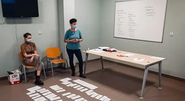 Trening zastępowania agresji: dwie kobiety w maseczkach, tablica z zapiskami, kartki na podłodze.