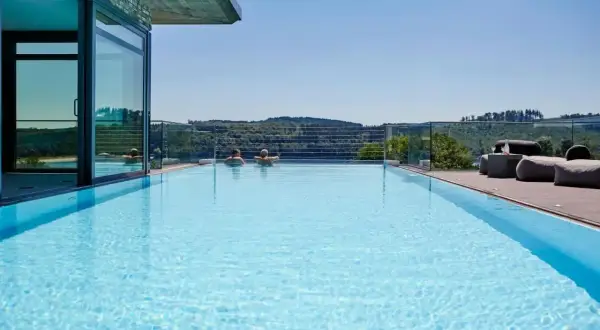 Traumpool mit Blick ins Grüne – perfekter Urlaub in NRW. Zwei Personen genießen das Wasser, während sich im Hintergrund sanfte Hügel erstrecken.