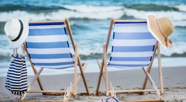 Dwa leżaki na plaży, gotowe na idealny weekend nad morzem. W tle widać morze i fale.