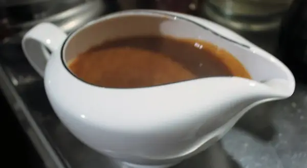 Eine weiße Sauciere gefüllt mit brauner Marsalasauce.