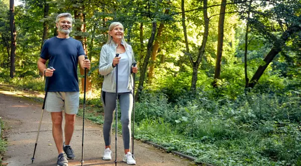 Älteres Paar genießt Nordic Walking im Wald. Eine gute Aktivität bei Bandscheibenvorfall zur Stärkung der Rückenmuskulatur.