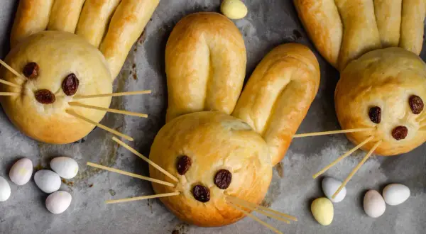 Osterhasen backen mit Hefeteig: Süße Hasen aus Teig mit Rosinenaugen und Spaghetti-Schnurrhaaren, umgeben von bunten Ostereiern.